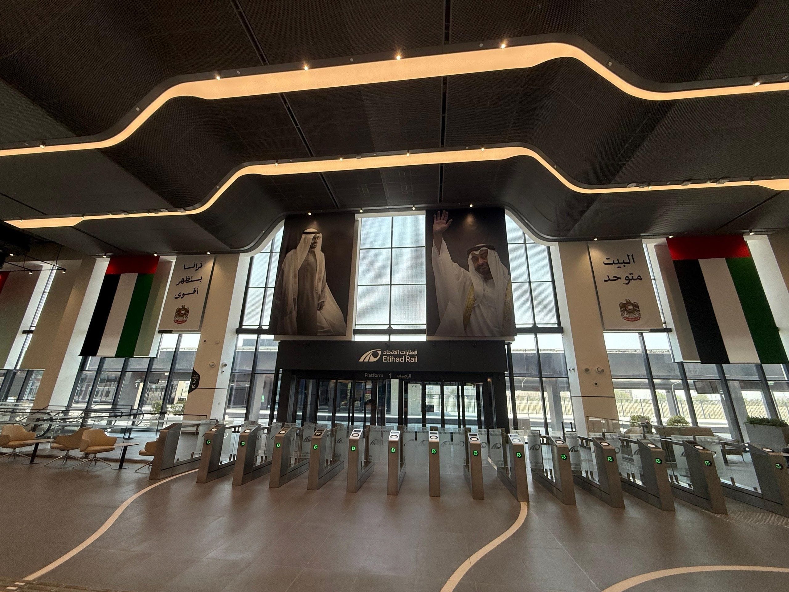 The ticket-gate hall of an Etihad Rail station, with the entrance to Platform 1 beneath portraits of the UAE's leaders
