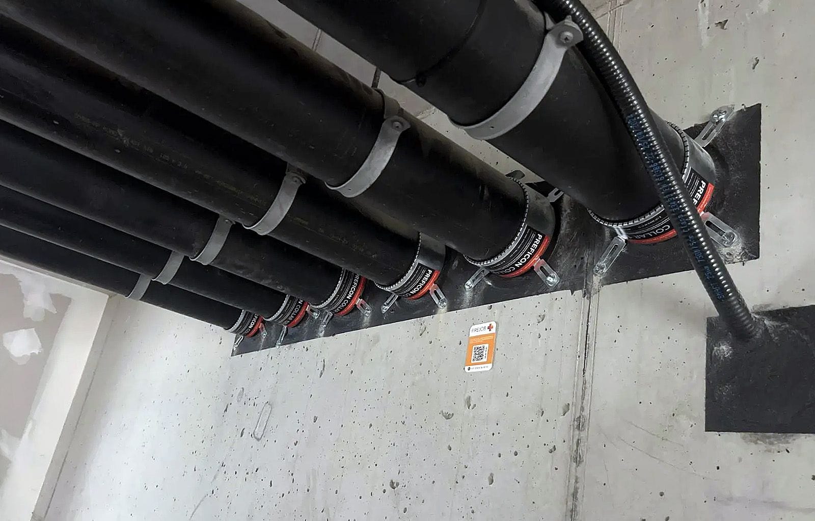 Row of fire-sealed pipe penetrations along a wall with a FIREJOB QR label recording the whole run