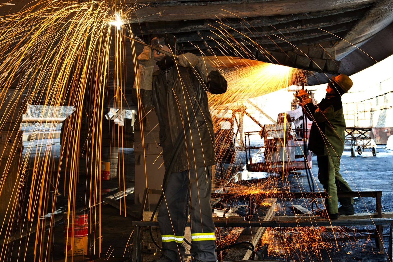 Shipyard workers grinding a vessel hull, sparks flying, during ship construction